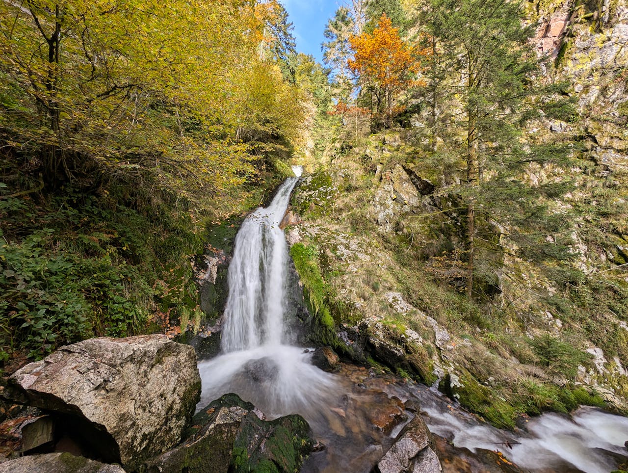 Beautiful autumn waterfall in Oppenau, Black Forest, Germany surrounded by lush foliage.